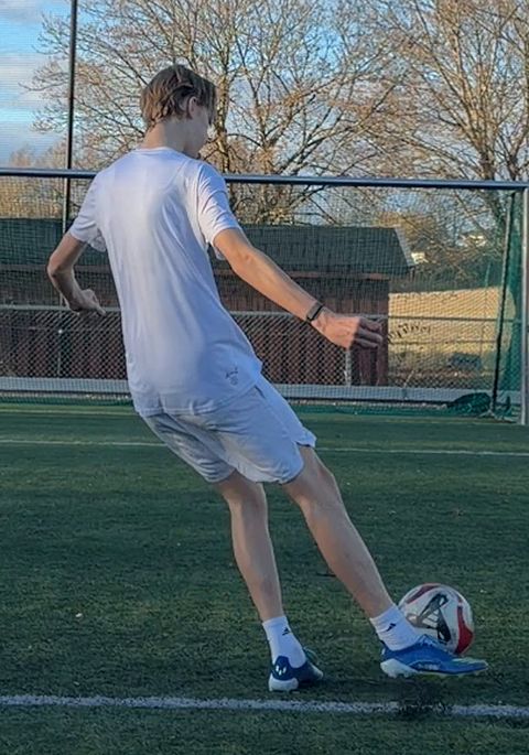 From behind at the strike: the shooting foot at the ball, arms out